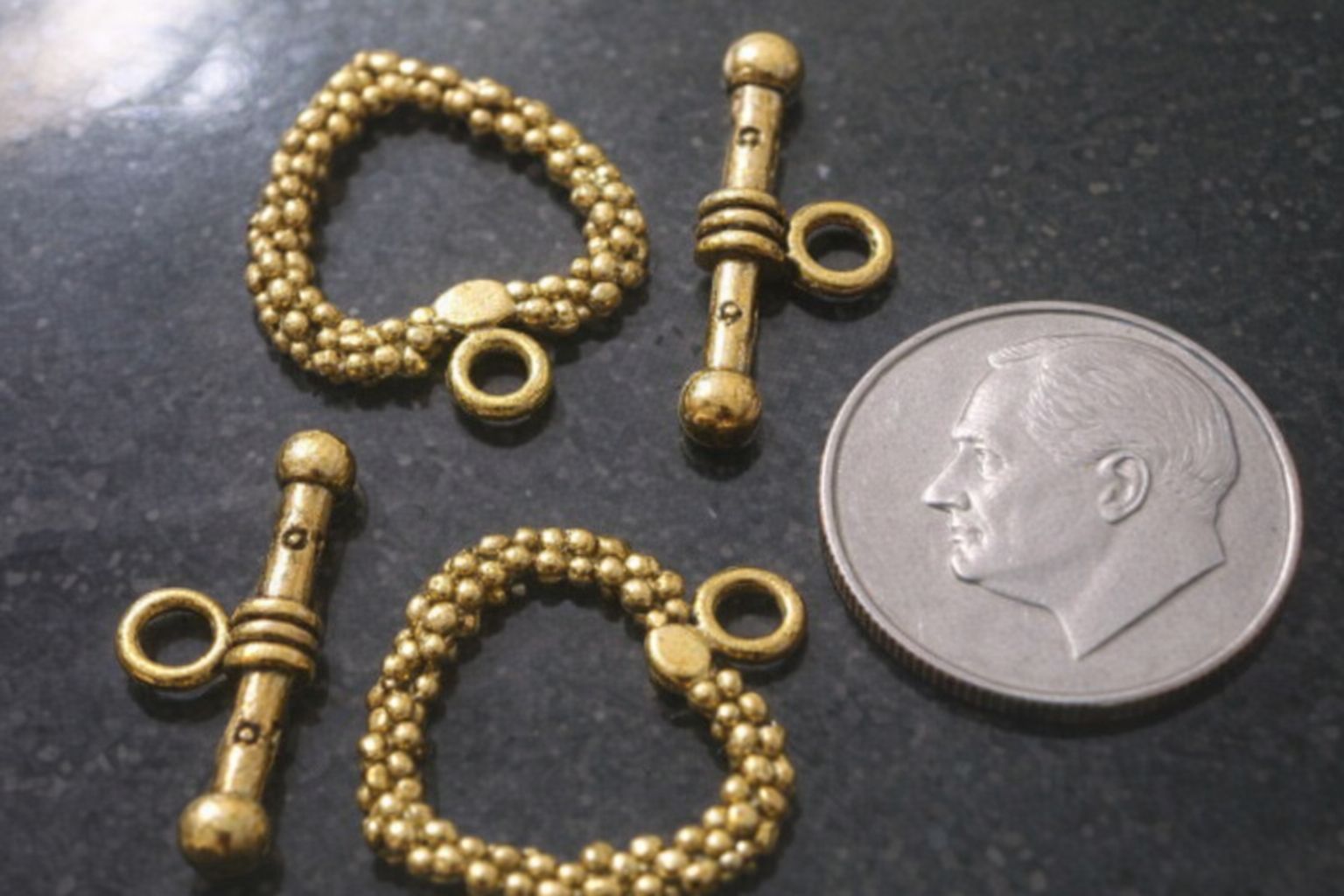 Guldfärgade toggle-lås bredvid ett silvermynt för storleksreferens.